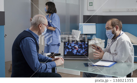 Physician explaining coronavirus spreading with illustration on laptop, giving medical advice to elder man at checkup visit. Medic and patient looking at virus animation on display. Physician explaining coronavirus spreading with illustration on laptop, giving medical advice to elder man at checkup visit. Medic and patient looking at virus animation on display. 138021355