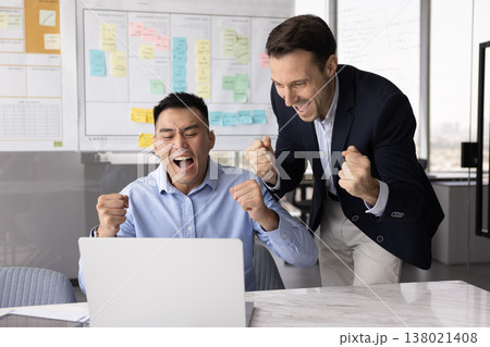 Excited diverse colleagues shout yes raise fists looking at notebook 138021408