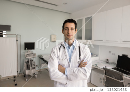 Doctor in white coat stands in modern medical examination room Doctor in white coat stands in modern medical examination room 138021488