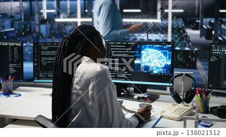 Female technician in data center answers telephone call, assisting users with AI troubleshooting. Server hub IT worker talks in phone call, managing customers issues using deep learning, camera A Female technician in data center answers telephone call, assisting users with AI troubleshooting. Server hub IT worker talks in phone call, managing customers issues using deep learning, camera A 138021512