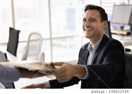 Happy mid adult businessman getting paper package sitting at desk 138021534