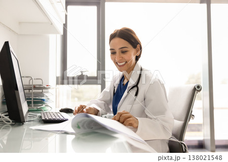 Young female doctor in uniform working seated at workplace table 138021548