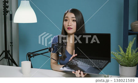 Asian woman reviewing laptop computer on social media podcast, recording live network video. Female vlogger broadcasting product recommendation with modern gadget and online technology. Asian woman reviewing laptop computer on social media podcast, recording live network video. Female vlogger broadcasting product recommendation with modern gadget and online technology. 138021589