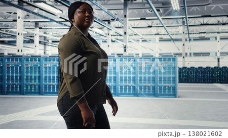 Data center admin conducts security audits to protect against cyber threats and vulnerabilities. Woman walking in server room, ensuring compliance with industry standards, camera A Data center admin conducts security audits to protect against cyber threats and vulnerabilities. Woman walking in server room, ensuring compliance with industry standards, camera A 138021602