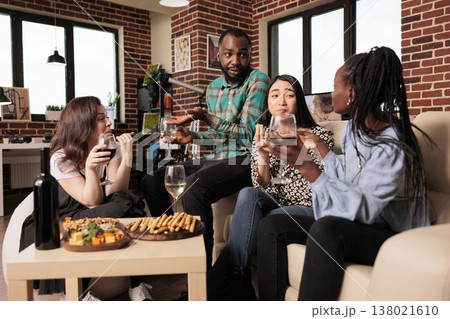 Culturally diverse friends talking, conversing each other, drinking wine, eating, tasting cheese, bread sticks at diverse people gathering. Different nationalities mates enjoying social life. 138021610