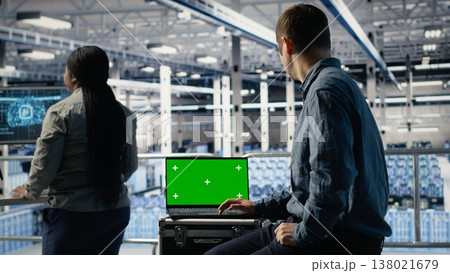 Data center IT experts investigate AI configurations using green screen laptop, making adjustments. Server hub engineers check deep learning errors on chroma key notebook, camera B 138021679