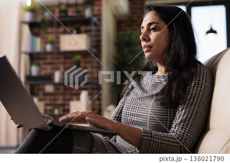 Business woman sitting on couch and working, doing remote office job on laptop pc at home. Using computer to work on data report, sending email and browsing internet for research plan. 138021790