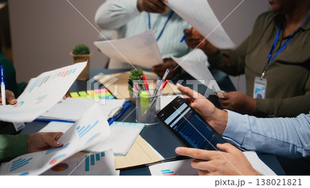 Close up of diverse staff collaborating on data forecasting and analysis, exchanging documents late in the office. Updating stakeholders with predictions and other business intel. Camera A. Close up of diverse staff collaborating on data forecasting and analysis, exchanging documents late in the office. Updating stakeholders with predictions and other business intel. Camera A. 138021821