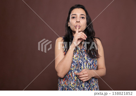 Indian woman showing silence gesture, making tsss sign portrait, front view. Girl looking at camera with forefinger on lips, attractive person keeping secret, studio mid shot 138021852