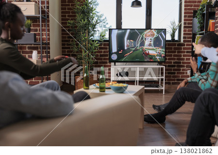 Diverse people playing video games competition on tv, enjoying shooting game play on console at hangout with friends. Having fun with shooter strategy, leisure activity with alcohol. 138021862