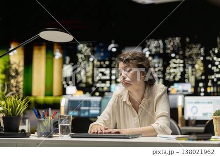 Businesswoman sleepy and demotivated at office desk after hours, experiencing workplace challenges and fatigue. Discouraged adult struggling with negative thoughts at night. Copy space. Businesswoman sleepy and demotivated at office desk after hours, experiencing workplace challenges and fatigue. Discouraged adult struggling with negative thoughts at night. Copy space. 138021962