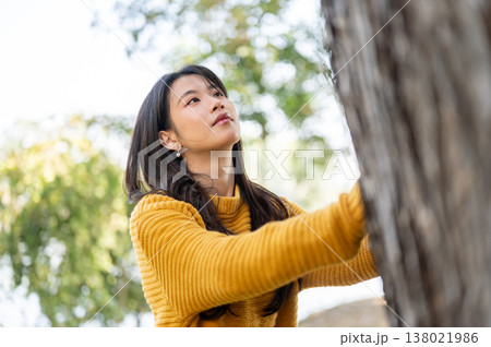Pretty asian woman in yellow sweater looking and touching on tree while standing in forest or park. Pretty asian woman in yellow sweater looking and touching on tree while standing in forest or park. 138021986
