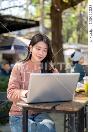 Pretty asian woman typing or looking at laptop aside green tea drink while sits at wooden cafe table 138022028