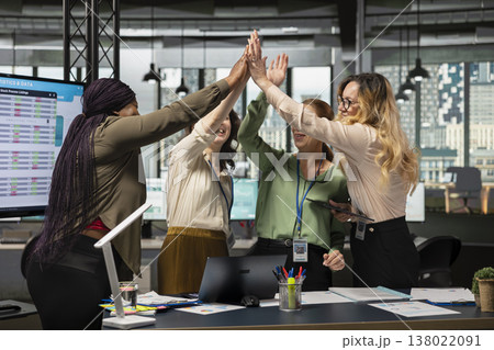 Multiethnic colleagues sharing a high five and celebrating their team success, feeling pleased with their victory and achievement in developing the company activity. Office accomplishment. Multiethnic colleagues sharing a high five and celebrating their team success, feeling pleased with their victory and achievement in developing the company activity. Office accomplishment. 138022091
