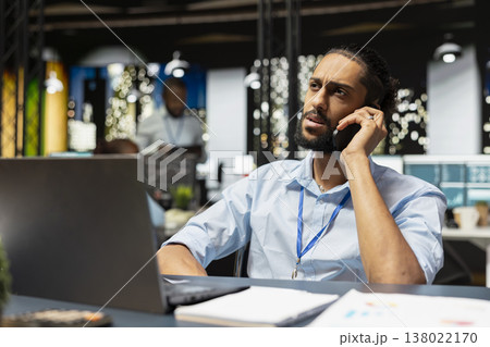 Worker at office desk answering telephone call from manager evaluating operational metrics. Staff member working late at night using mobile phone to assist online clients during call Worker at office desk answering telephone call from manager evaluating operational metrics. Staff member working late at night using mobile phone to assist online clients during call 138022170