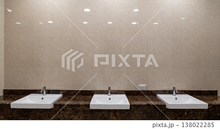 Modern restroom interior featuring multiple sinks aligned in a row representing hygiene standards and public facility design. 138022285