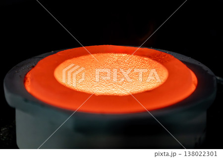 Close up of molten metal being poured into a heated crucible during casting showing intense heat, flame, and thermal energy. 138022301