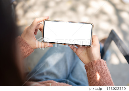Close up of woman holding white screen phone horizontally sits on outdoor bench over concrete floor. 138022330