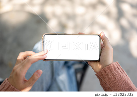 A woman's hand holding and touching white screen phone sitting on outdoor bench over concrete floor. 138022332