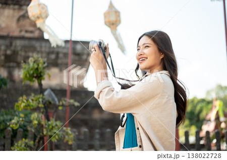Pretty asian woman raising camera looking around while standing at ancient pagoda in buddhist temple 138022728