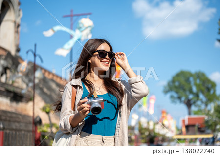 A woman holding sunglasses and camera standing or walking around ancient pagoda of buddhist temple. A woman holding sunglasses and camera standing or walking around ancient pagoda of buddhist temple. 138022740