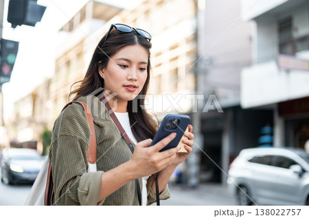 Pretty asian woman holding coffee looking at phone while standing or walking by street road in town Pretty asian woman holding coffee looking at phone while standing or walking by street road in town 138022757