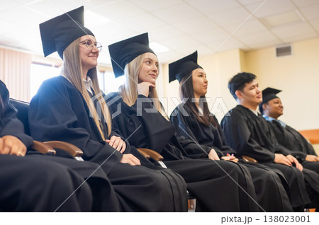 Young people in graduation gowns listen to a speech.  138023001