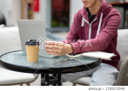 Close up of man student freelancer holding screen look at laptop aside book and coffee at cafe table Close up of man student freelancer holding screen look at laptop aside book and coffee at cafe table 138023046