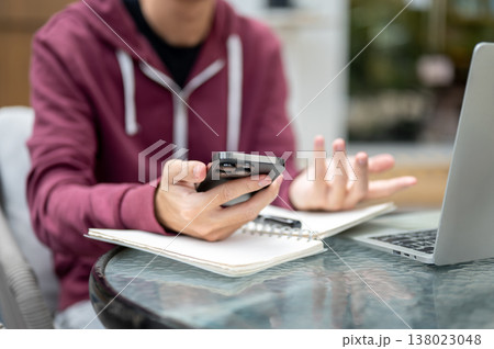 Close up of man student freelancer looking confused at smartphone over book and laptop at cafe table Close up of man student freelancer looking confused at smartphone over book and laptop at cafe table 138023048