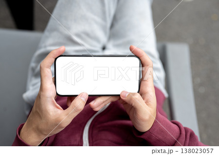 Top view of man holding white screen phone watching video playing game on chair over concrete floor. Top view of man holding white screen phone watching video playing game on chair over concrete floor. 138023057