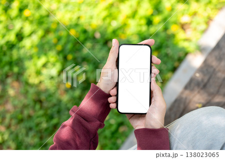 Top view close up of a man holding white screen phone with both hands while sitting at garden park. 138023065