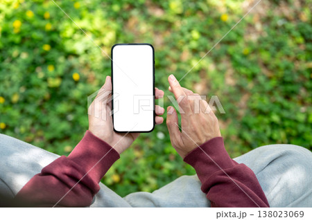 Top view of a hand holding white screen phone with fingers pointing sits over grass at garden park. Top view of a hand holding white screen phone with fingers pointing sits over grass at garden park. 138023069