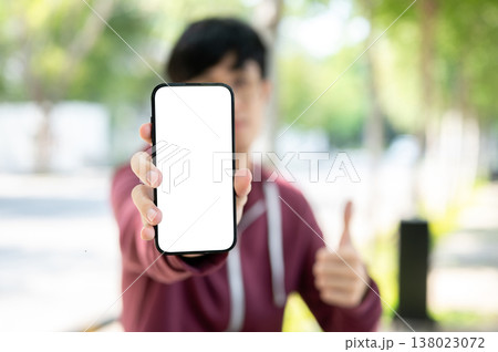 Blurred man holding and showing white screen phone as giving thump up while sitting at garden park. Blurred man holding and showing white screen phone as giving thump up while sitting at garden park. 138023072