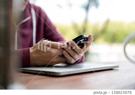 Close up of a man student freelancer holding or looking at phone while sits at wooden table in cafe Close up of a man student freelancer holding or looking at phone while sits at wooden table in cafe 138023078