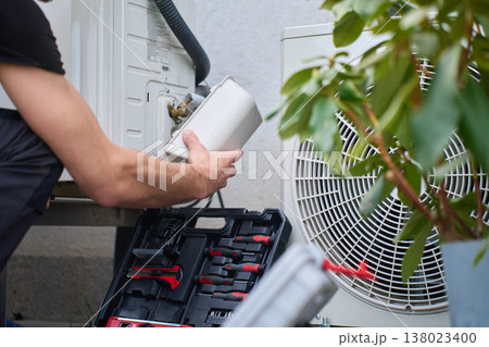 Technician servicing outdoor heat pump unit at residential house Technician servicing outdoor heat pump unit at residential house 138023400