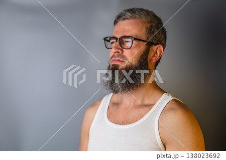 Man with glasses and beard stands against a gray wall in a tank top Man with glasses and beard stands against a gray wall in a tank top 138023692