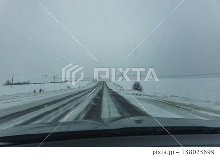 Snowy road stretches ahead through winter landscape in cold weather Snowy road stretches ahead through winter landscape in cold weather 138023699