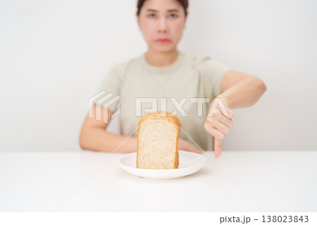Unhappy woman showing thumbs down gesture and refusing to eat bread. concept of gluten intolerance, gluten sensitivity, carb loading concerns, or a disliking for unhealthy dietary habits Unhappy woman showing thumbs down gesture and refusing to eat bread. concept of gluten intolerance, gluten sensitivity, carb loading concerns, or a disliking for unhealthy dietary habits 138023843