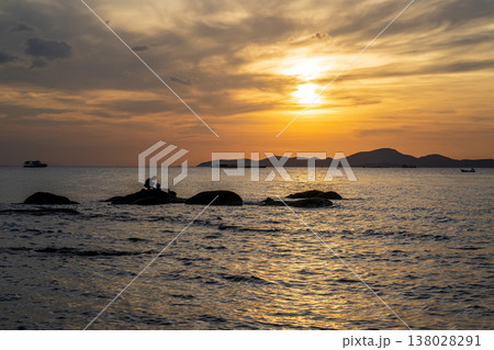 Seaside Fisherman Sitting on Rocks at Sunset 138028291