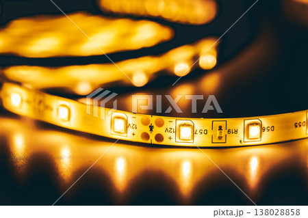 Glowing LED strip light close-up on dark background, warm light technology Glowing LED strip light close-up on dark background, warm light technology 138028858