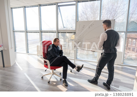 Two Caucasian men discussing work at a white board. Two Caucasian men discussing work at a white board. 138028891