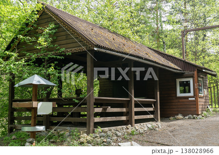 Rustic Wooden Cabin Shelter In Lush Forest Park With Covered Porch And Gravel Path 138028966