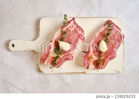 Raw pork rib chop with garlic and herbs prepared on a cutting board in a kitchen setting Raw pork rib chop with garlic and herbs prepared on a cutting board in a kitchen setting 138029235