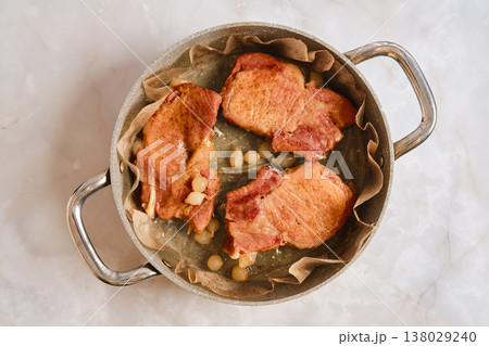 Roasted pork rib chop cooking in a pot with onions on a marble kitchen countertop Roasted pork rib chop cooking in a pot with onions on a marble kitchen countertop 138029240
