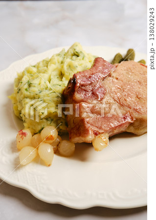 Pork rib chop served with mashed potatoes and pickles on a white plate with a side of onions Pork rib chop served with mashed potatoes and pickles on a white plate with a side of onions 138029243