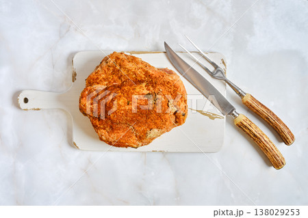 Looking at a pork shoulder on a cutting board with carving tools on a light surface Looking at a pork shoulder on a cutting board with carving tools on a light surface 138029253