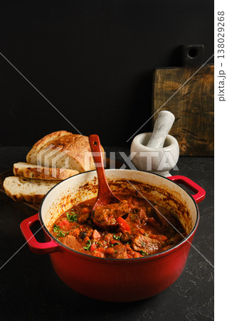 Beef stew in a red pot with bread and mortar background in a kitchen setting Beef stew in a red pot with bread and mortar background in a kitchen setting 138029268