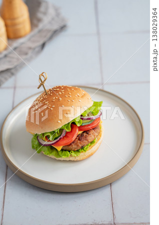 Meat burger with tomato, cheese, and lettuce on a plate on a kitchen table with spice and napkin. Meat burger with tomato, cheese, and lettuce on a plate on a kitchen table with spice and napkin. 138029364