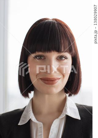 A confident businesswoman with a bob haircut and professional attire smiles warmly, conveying approachability and competence in a corporate setting 138029907