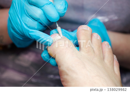 Professional Pedicure Treatment. Nail Technician Using Electric Drill on Toenails in Beauty Salon with Blue Gloves. Care and cosmetic treatment with proper hygiene standards.  138029982